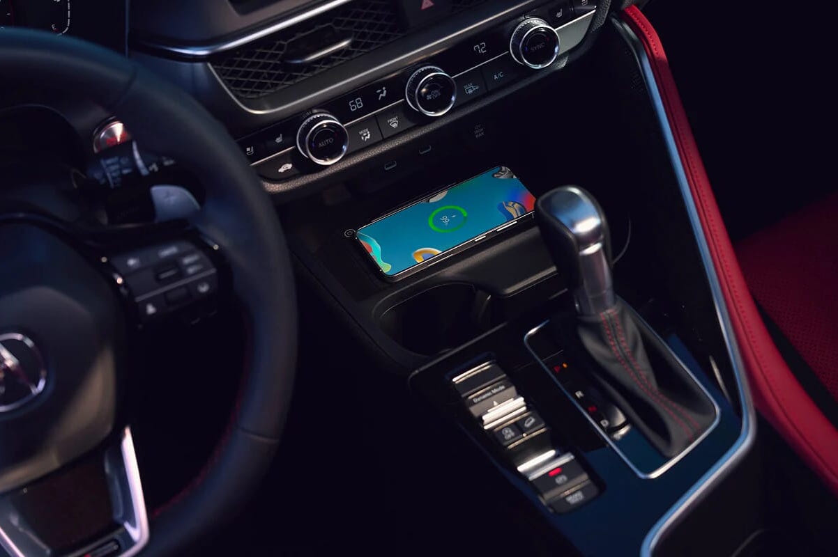 2026 Acura ADX interior with a sleek dashboard displaying climate controls, a gear shift, and a smartphone showing a colorful charging screen, conveying modern technology.
