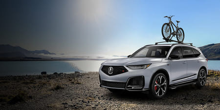 A silver 2026 MDX parked by a lake with a bike mounted on the roof.