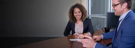 Smiling woman and man in suits review documents at an office table, conveying a friendly, productive business meeting.