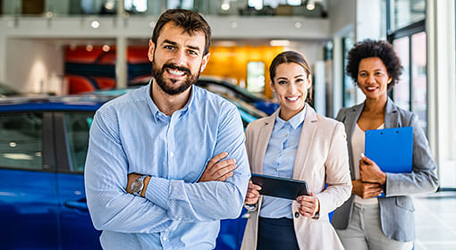 Group of smiling car dealers in vehicle showroom