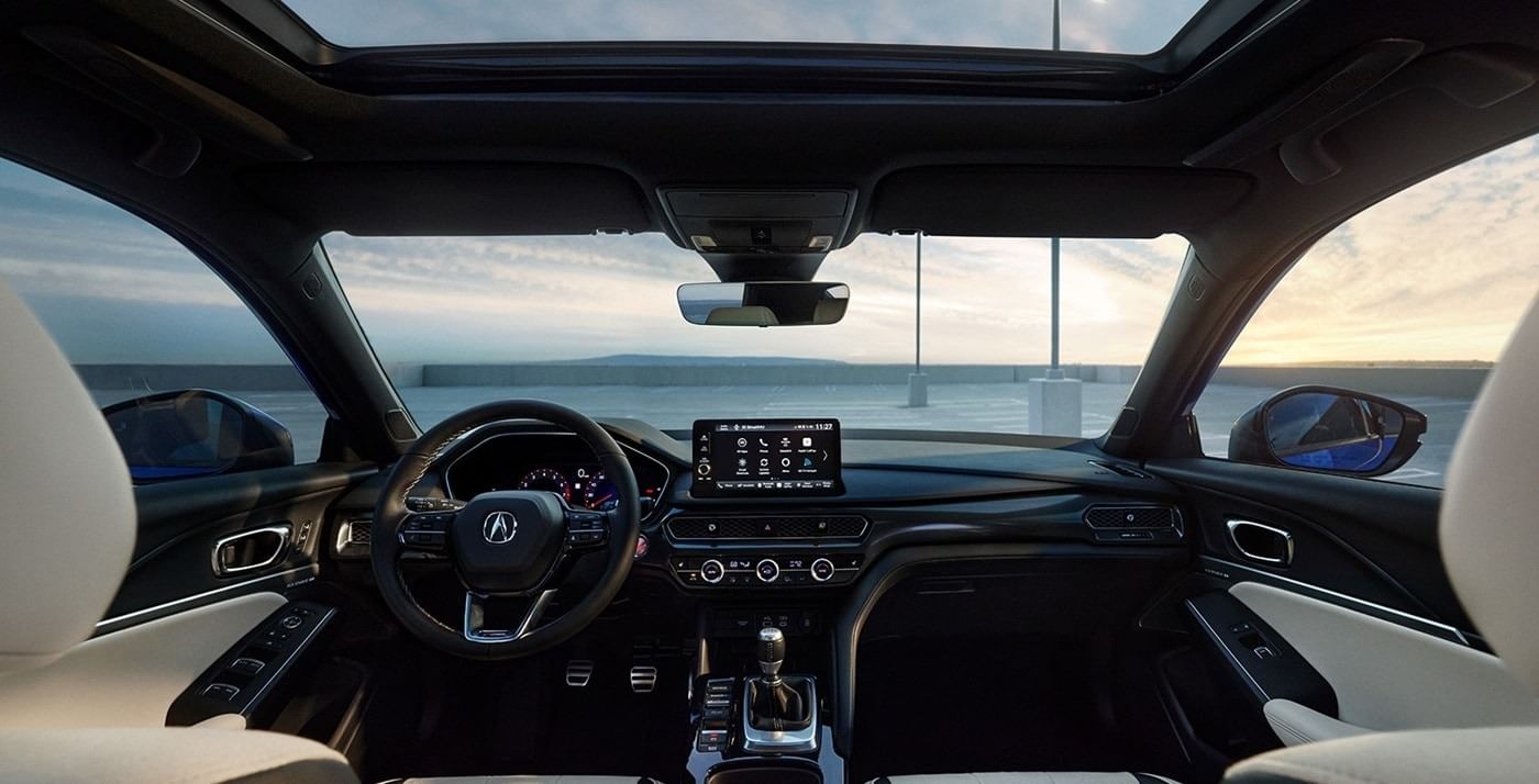 Interior view of an 2025 Acura Integra with a sleek dashboard, touchscreen display, and panoramic sunroof, showcasing modern design and technology.