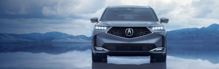 A gray Acura MDX parked on a reflective surface with mountains in the background.