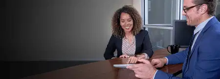 Smiling woman and man in suits review documents at an office table, conveying a friendly, productive business meeting.