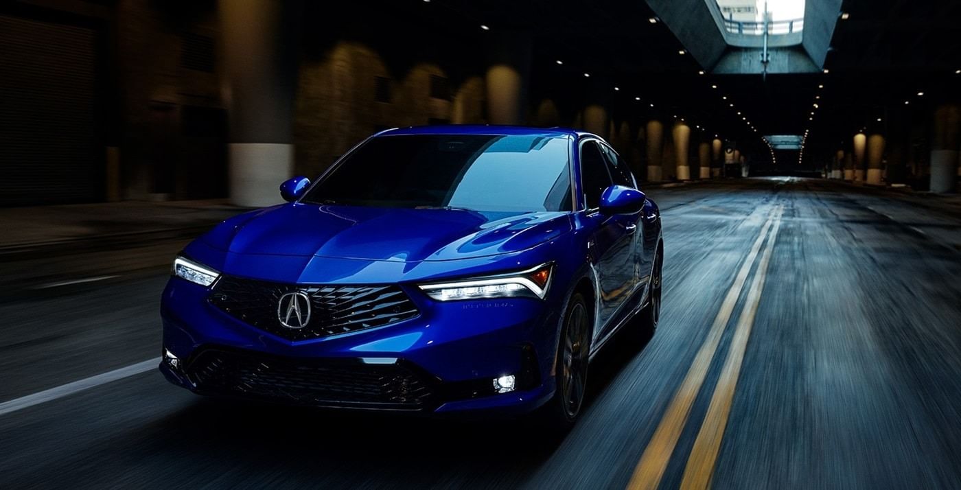 A sleek blue 2025 Acura Integra car speeds through a dimly lit urban tunnel, showcasing its modern design and glossy finish.