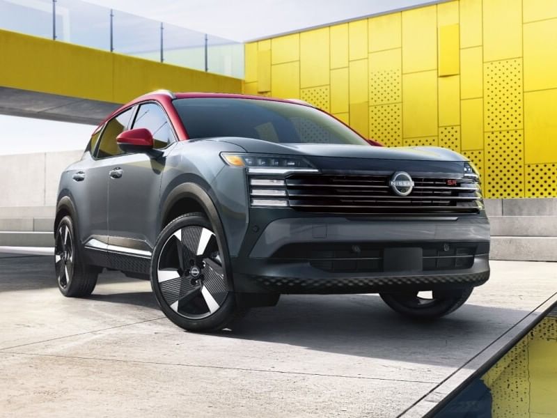 A sleek gray 2026 Nissan Kicks with a red roof and stylish black wheels, parked against a modern yellow and concrete backdrop.