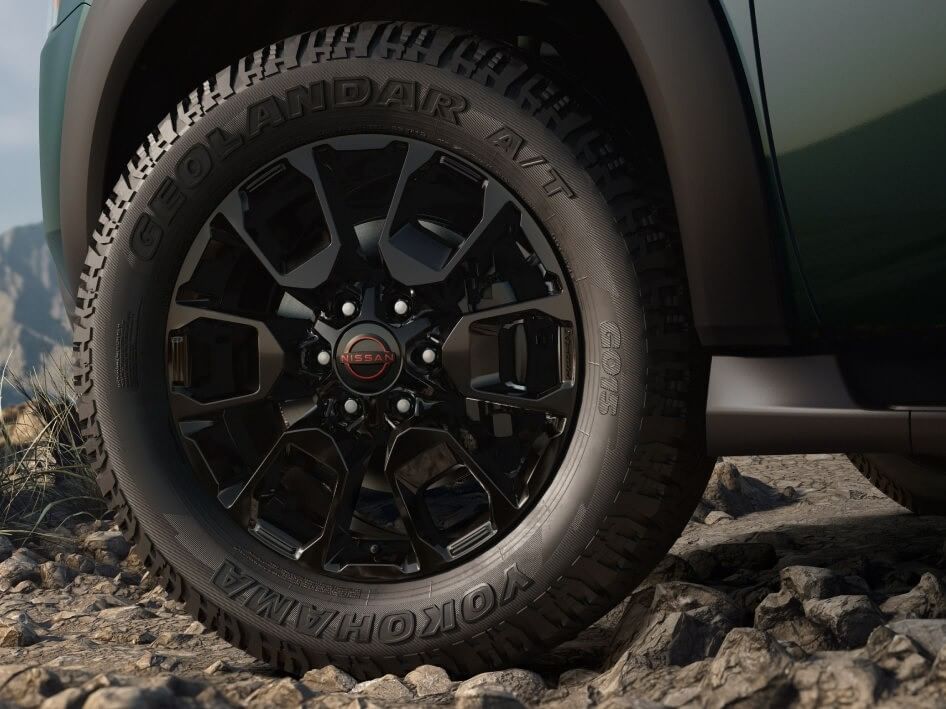 Close-up of a black alloy wheel on a 2026 Nissan Armada, showcasing a Yokohama Geolandar A/T tire on rocky terrain.