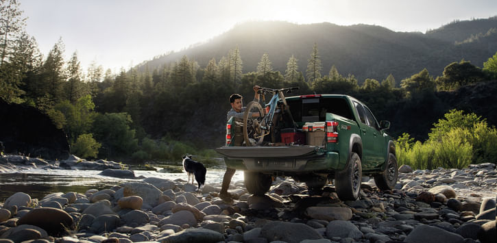 2026 Frontier at a mountain stream; the driver is adjusting cargo in the back.