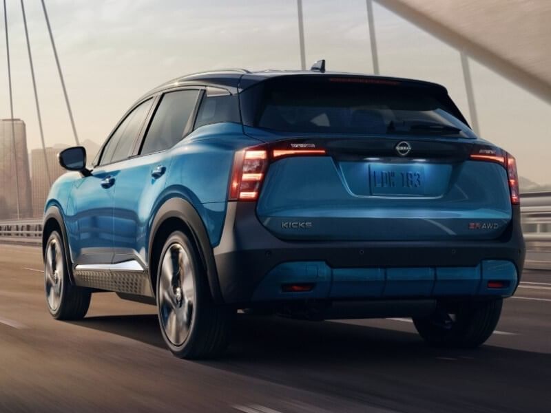 A blue 2026 Nissan Kicks in motion on a bridge, showcasing its sleek rear design and urban backdrop at twilight.