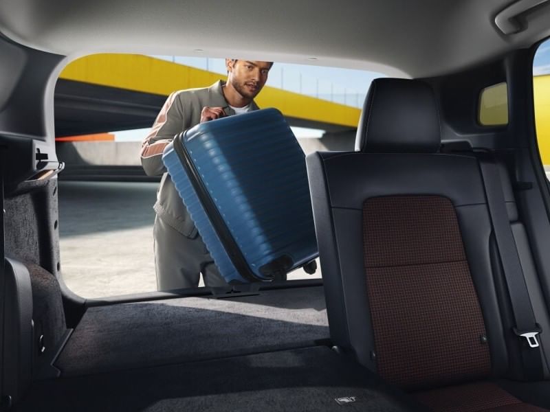 A man carrying a suitcase to the back of a 2026 Nissan Kicks, indicating he is about to travel or go on a trip.