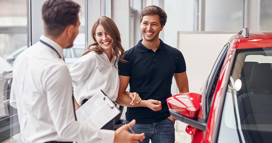 Salesman is talking with a couple next to red car