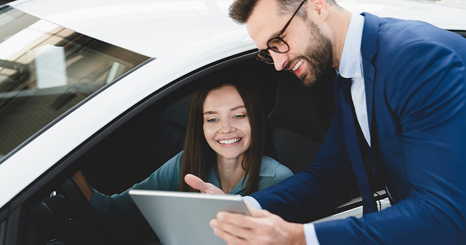 A man shows a tablet to a woman sitting in the driver's seat