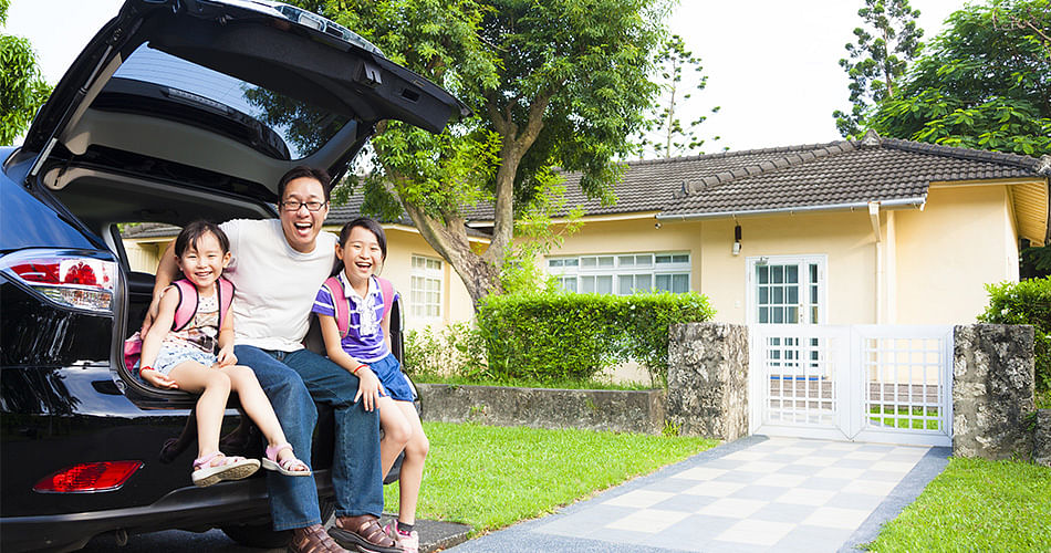 Happy family is sitting on the open car trunk in front of the house