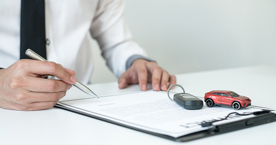 A person in a suit signs a document with a miniature car model and car keys lying on it