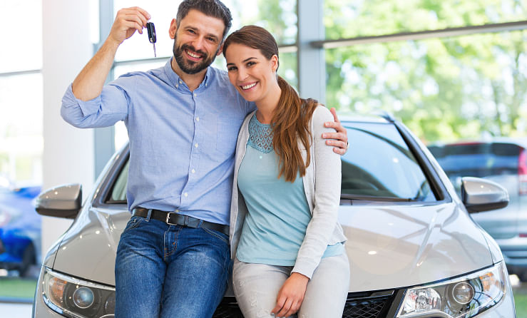 Couple leaning on the car they just purchased while holding the key in their hand