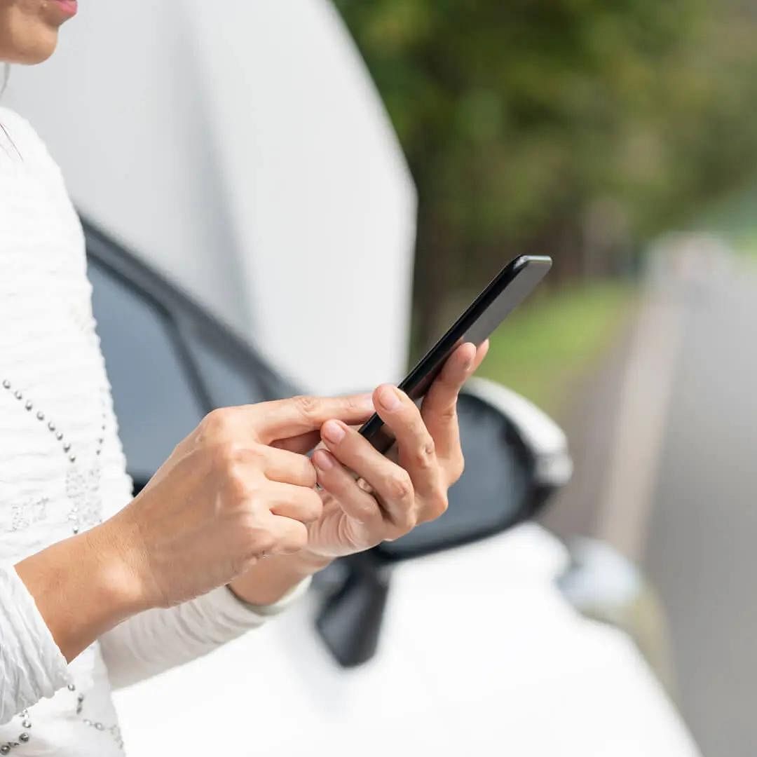 Woman using a smartphone, in the background a car with an open hood