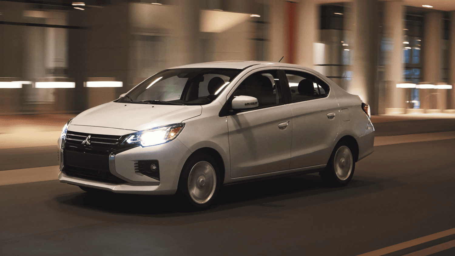 White 2024 Mitsubishi Mirage G4 sedan driving through city streets near Valrico, FL with its headlights on.
