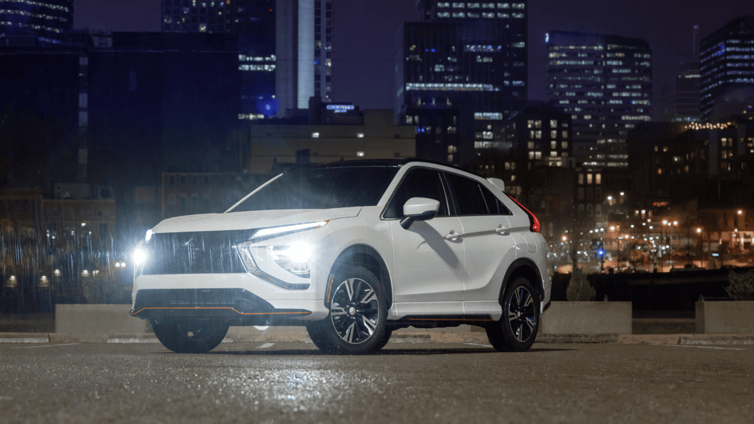 White 2025 Mitsubishi Eclipse Cross parked at night with city lights in Valrico, FL, highlighting its sleek LED headlights.