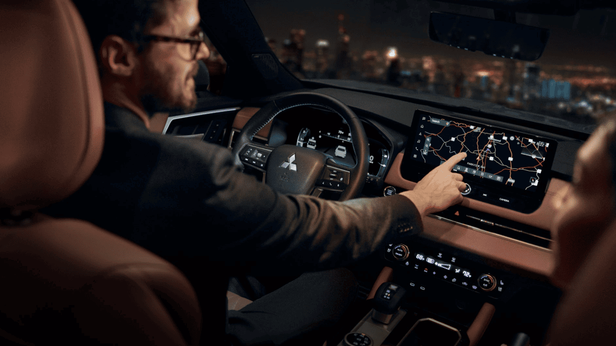 Man navigating the touchscreen display in the 2025 Mitsubishi Outlander PHEV near Tampa, FL, with city lights in the background.