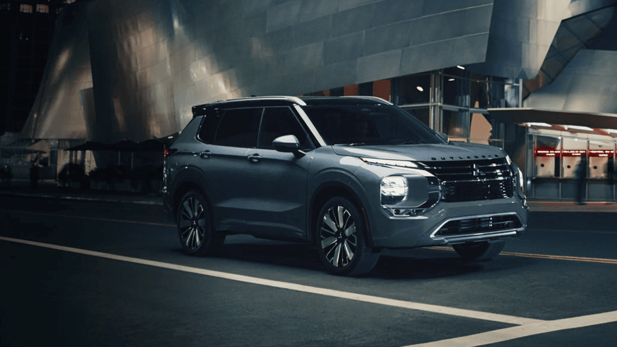 The 2025 Mitsubishi Outlander near Riverview, FL, parked in a vibrant nighttime cityscape with its LED headlights illuminated, showcasing modern styling and upscale presence.