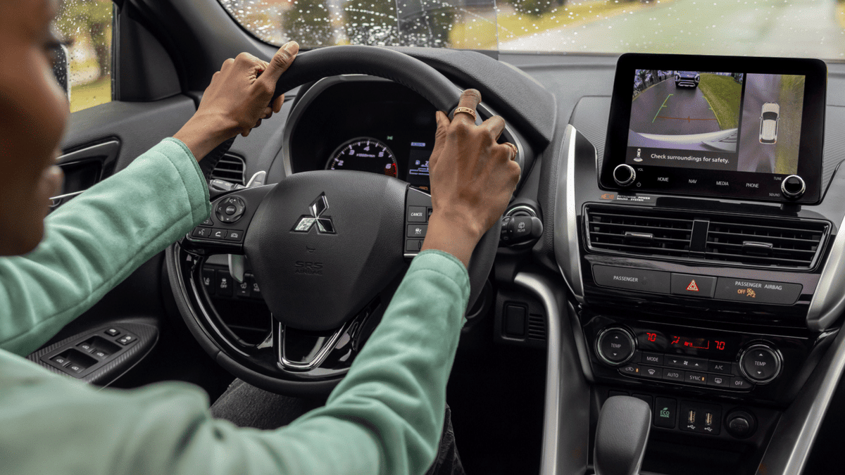 Driver's view inside the 2025 Mitsubishi Eclipse Cross, showing the digital rearview camera on the center screen and hands on the steering wheel, promoting high-tech safety and convenience features.