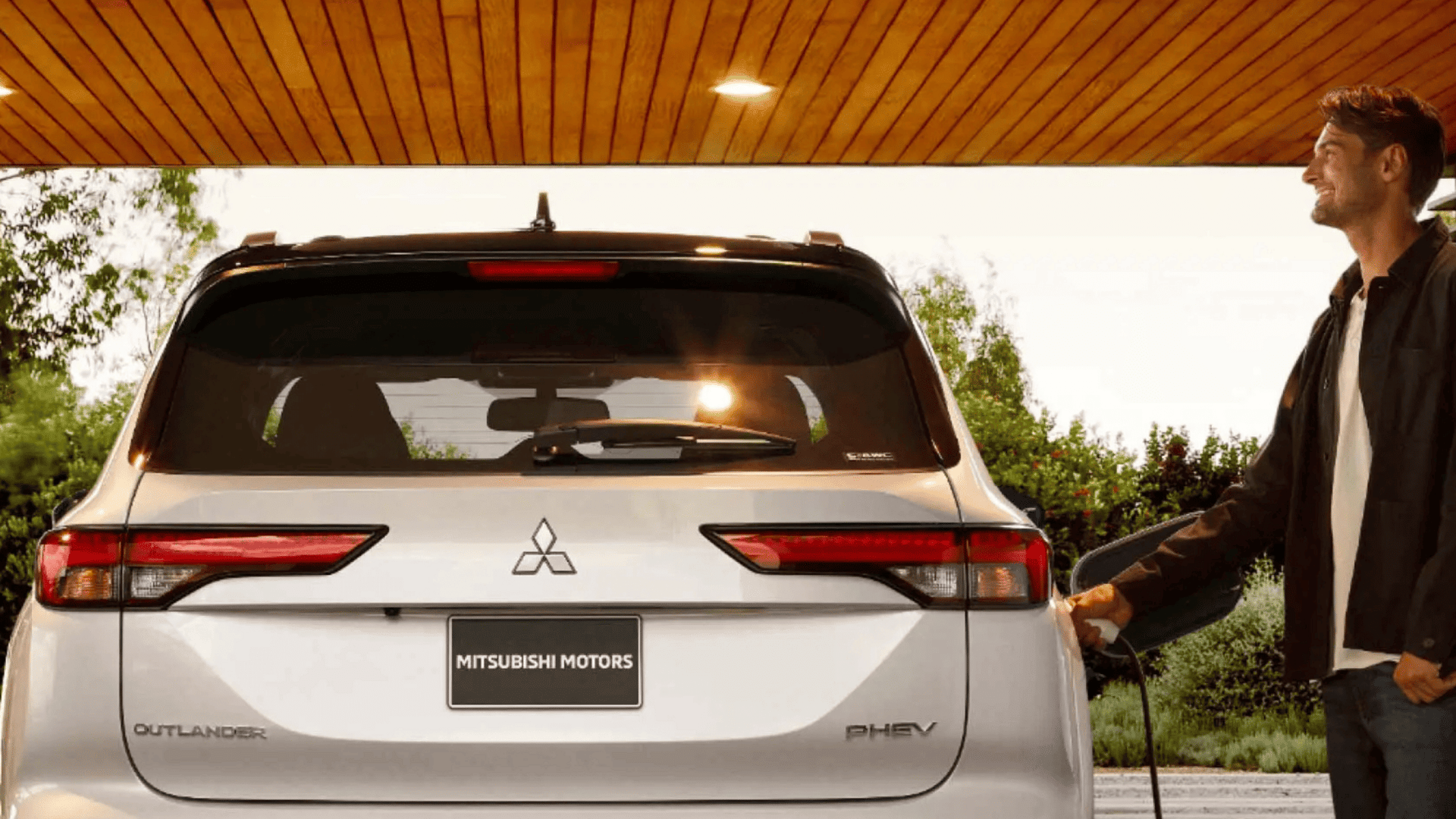 Rear view of 2025 Mitsubishi Outlander PHEV being charged by a man under wooden awning near Brandon, FL