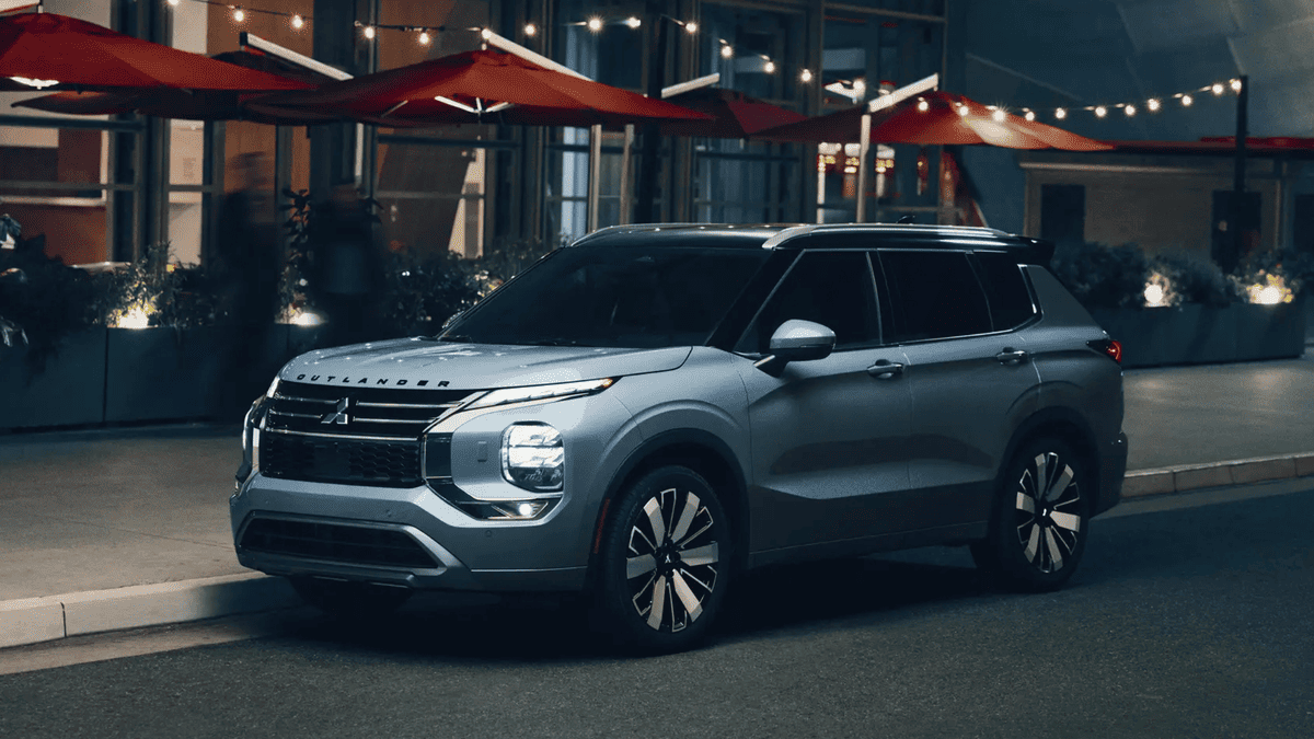 Night view of the 2025 Mitsubishi Outlander parked outside a restaurant in Tampa, FL, with headlights on and modern styling under ambient lighting.