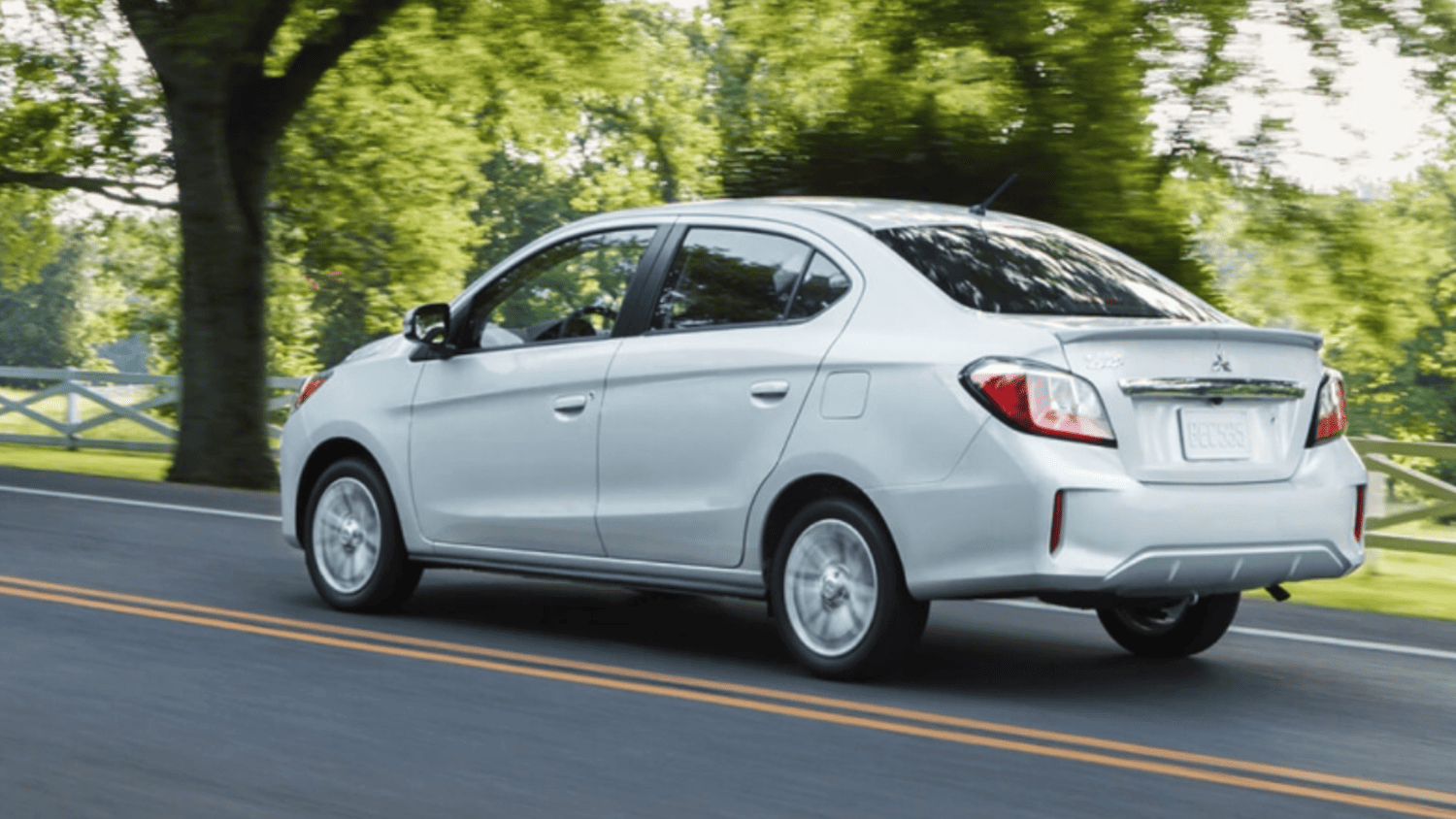Rear-angle driving shot of the 2024 Mitsubishi Mirage G4 sedan cruising on scenic roads near Lakeland, FL, emphasizing its fuel-efficient design.