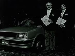 Two men stand beside a car.