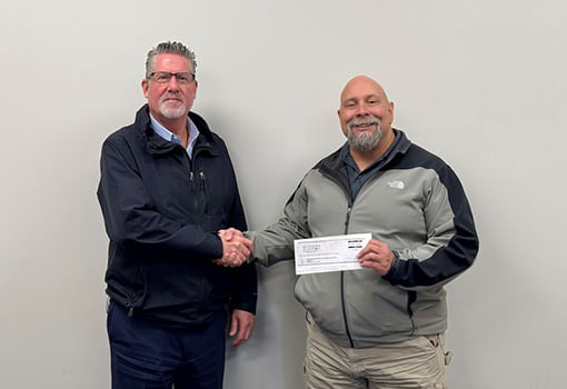 Dos hombres se dan la mano con un cheque, representando la donación de Canobie Lake para apoyar a los veteranos y sus familias.