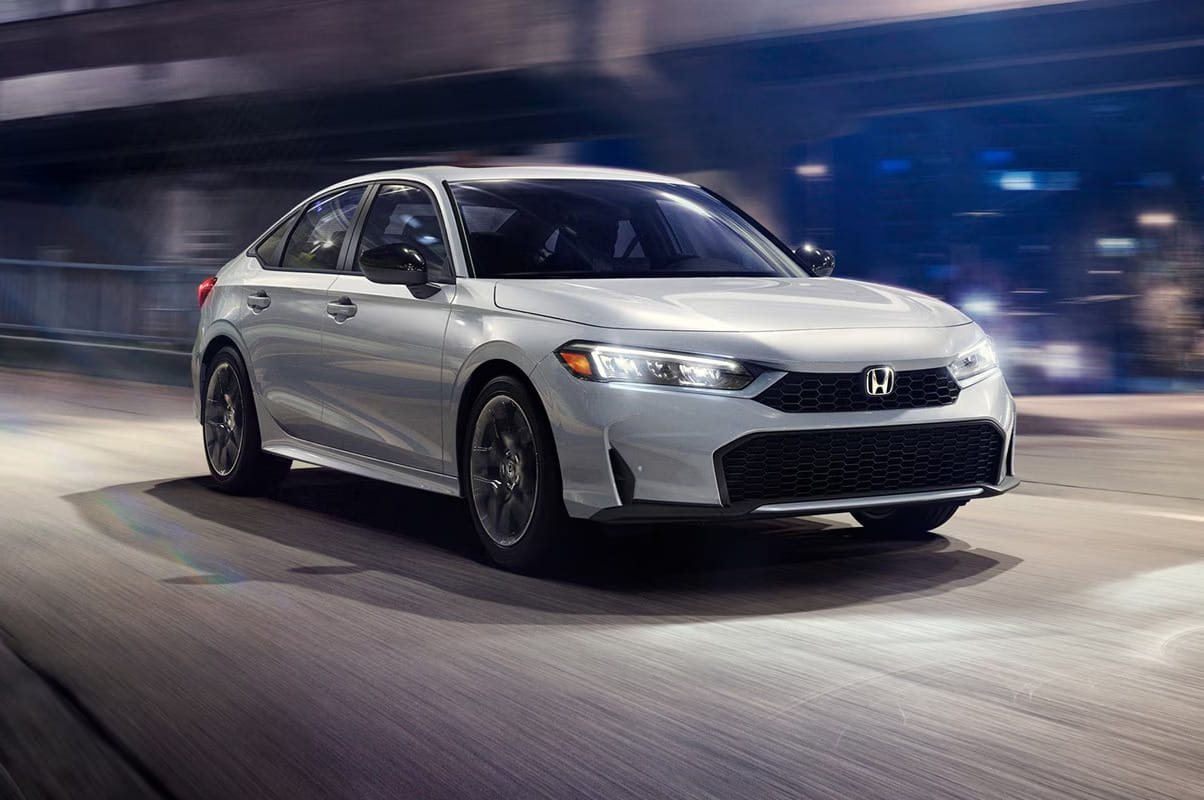 A sleek, silver 2026 Honda Civic Sedan drives dynamically through a city street at night, with blurred lights creating a sense of speed and modernity.