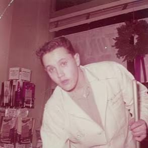 A vintage photo of a young man in a work coat leaning forward while holding a tool.