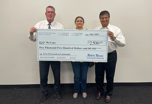 Tres personas sostienen con orgullo un cheque frente a una pared, apoyando la misión de We Care Charity de ayudar a familias necesitadas.