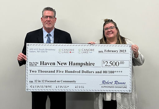 Dos personas sostienen con orgullo un cheque de $2,500 para apoyar los servicios de prevención de violencia y bienestar familiar de HAVEN New Hampshire.