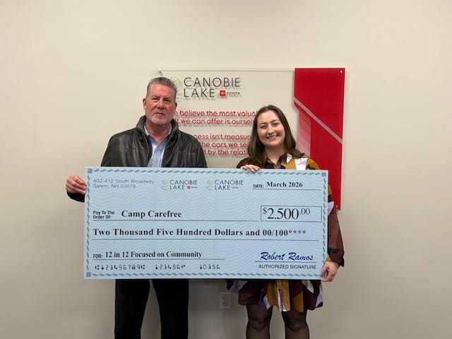 A man and a smiling woman stand side-by-side holding a large, light blue novelty presentation check. The check is from Canobie Lake Toyota and Canobie Lake Honda, dated March 2026, and is made payable to Camp Carefree for the amount of $2,500.