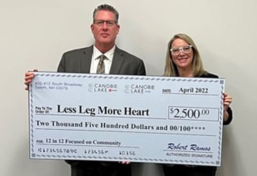 Dos personas muestran con orgullo un cheque de $2,500, representando la donación de Canobie Lake a Less Leg More Heart.