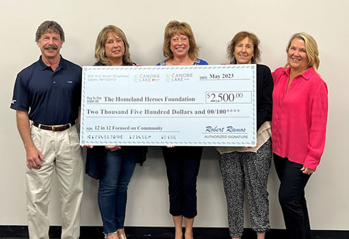 Cuatro personas sostienen con orgullo un cheque grande para la Homeland Heroes Foundation, apoyando a veteranos locales y sus familias.