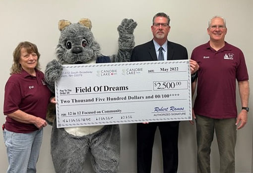 Tres personas paradas junto a un cheque grande, celebrando la donación de $2,500 de Canobie Lake a la organización The Field of Dreams