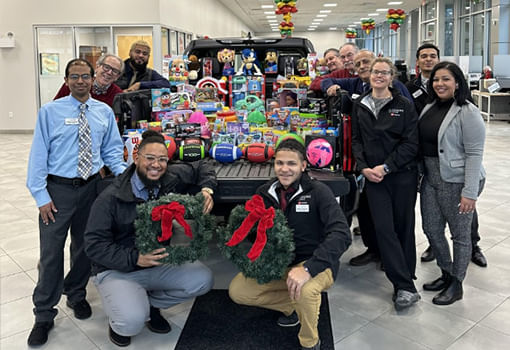 Un grupo de personas sonrientes se para junto a un camión lleno de juguetes coloridos, apoyando a la Marine Toys for Tots Foundation.