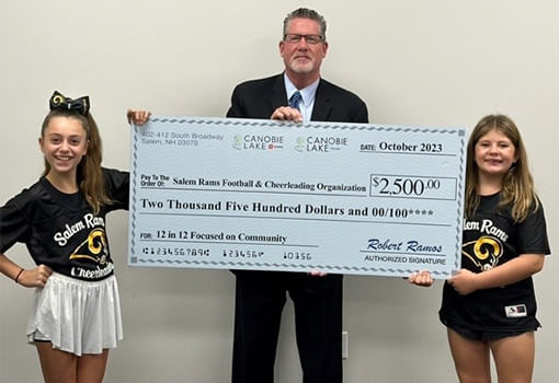 Dos niñas y un hombre sostienen con orgullo un cheque para la Organización de Fútbol Americano y Porristas Salem Rams de Canobie Lake Honda y Toyota.
