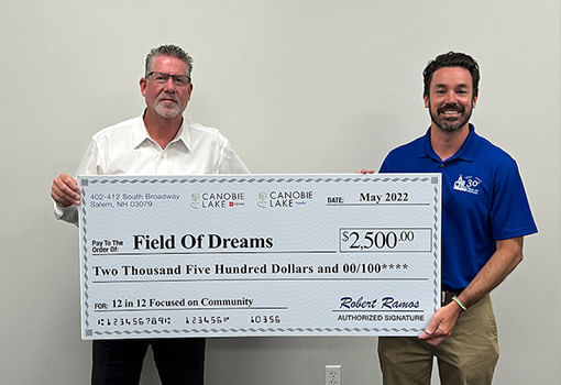 Dos hombres con un cheque de $2,500, mostrando el patrocinio de Canobie Lake Honda & Toyota a Field of Dreams en la comunidad.