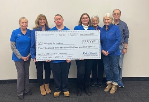 Un grupo con camisetas azules sostiene con orgullo un cheque, apoyando la misión de Bridging the Horizon para entretenimiento asequible para personas con necesidades especiales.