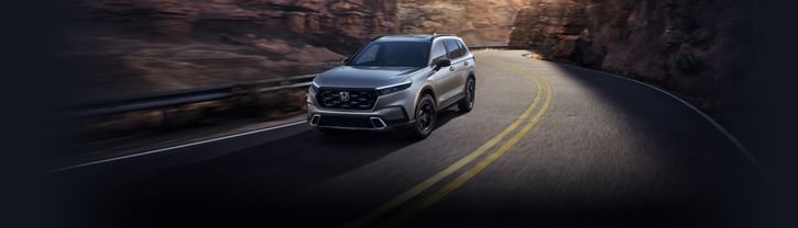 Un Honda CR-V Hybrid plateado de 2025 circula por una carretera sinuosa a través de un cañón con acantilados rocosos y un paisaje desértico de fondo.
