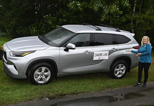 Una mujer se para junto a una Toyota Highlander plateada, mostrando el vehículo donado al Boys & Girls Club of Greater Salem.