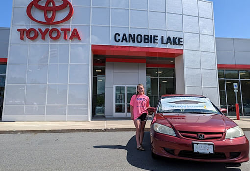 Una mujer se para con orgullo frente a un concesionario Toyota, celebrando una rifa de automóvil para graduados de Salem High School.