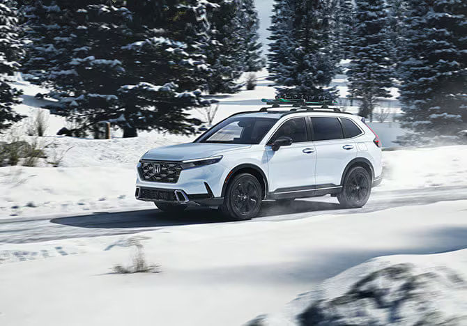 Honda CR-V 2025 blanco conduciendo en la nieve con portaesquís