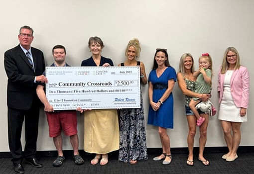 Un grupo de personas se para con orgullo frente a un cheque grande, celebrando la donación de Canobie Lake Honda a Community Crossroads.