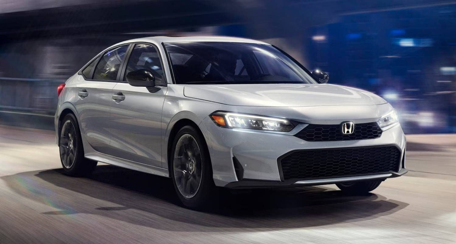 The 2025 Honda Civic Sedan LX in Solar Silver Metallic driving at night, with urban bridge and the city behind