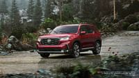 2023 Honda Pilot Elite in Radient Red Metallic II while driving in the rain in the wilderness. Forest in the background