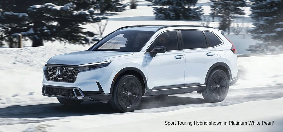 A Platinum White Pearl Honda Sport Touring Hybrid driving down a snowy road