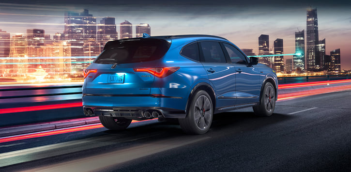 A blue 2026 MDX driving through the city at night.